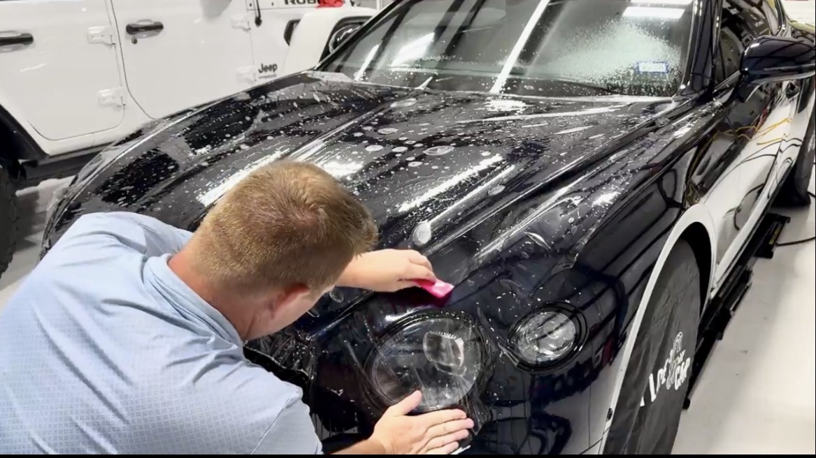 Paint protection film being installed on a black car hood